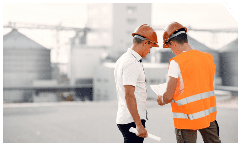 dos trabajadores mirando un plano con planta industrial de fondo