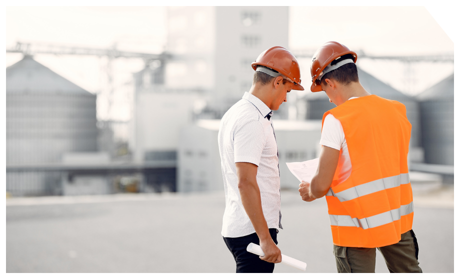 dos trabajadores mirando un plano con planta industrial de fondo